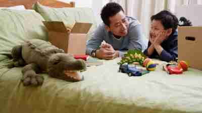 A dad helps his son with ADHD put toys in a box to clean up his messy bedroom.