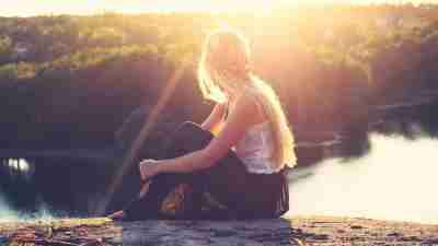 Woman with ADHD sitting on top of mountain overlooking lake at sunset thinking about her diagnosis