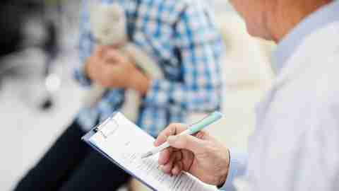 Closeup of doctor writing on clipboard while talking with a young patient with ADHD.