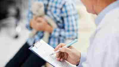 Closeup of doctor writing on clipboard while talking with a young patient with ADHD.