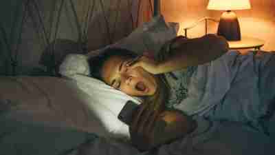 Girl lying in bed uses a cell phone and yawns