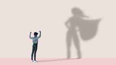 Woman flexing muscles in front of superhero shadow