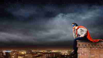 Young man in superhero costume sitting on top of building