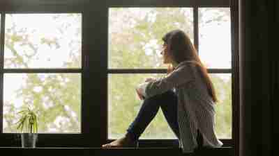 Thoughtful girl sitting on sill embracing knees looking at window, sad depressed teenager spending time alone at home, young upset pensive woman feeling lonely or frustrated thinking about problems