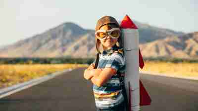 A young boy wearing flying goggles has a rocket strapped to his back as he is ready to fly to new imaginary places. Image taken in Utah, USA.