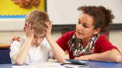 Stressed ADHD Schoolboy Studying In Classroom With Teacher