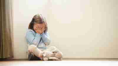 Little girl with ADHD sitting in corner with hands on face