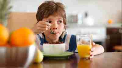 Cute boy with ADHD drinking orange juice and eating muesli for breakfast