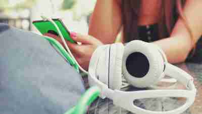 Teen girl with ADHD playing on smartphone with headphones and bag on table outside