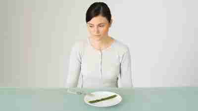 A young woman sits in front of an empty plate, looking uneasy, to represent eating disorders and adhd.